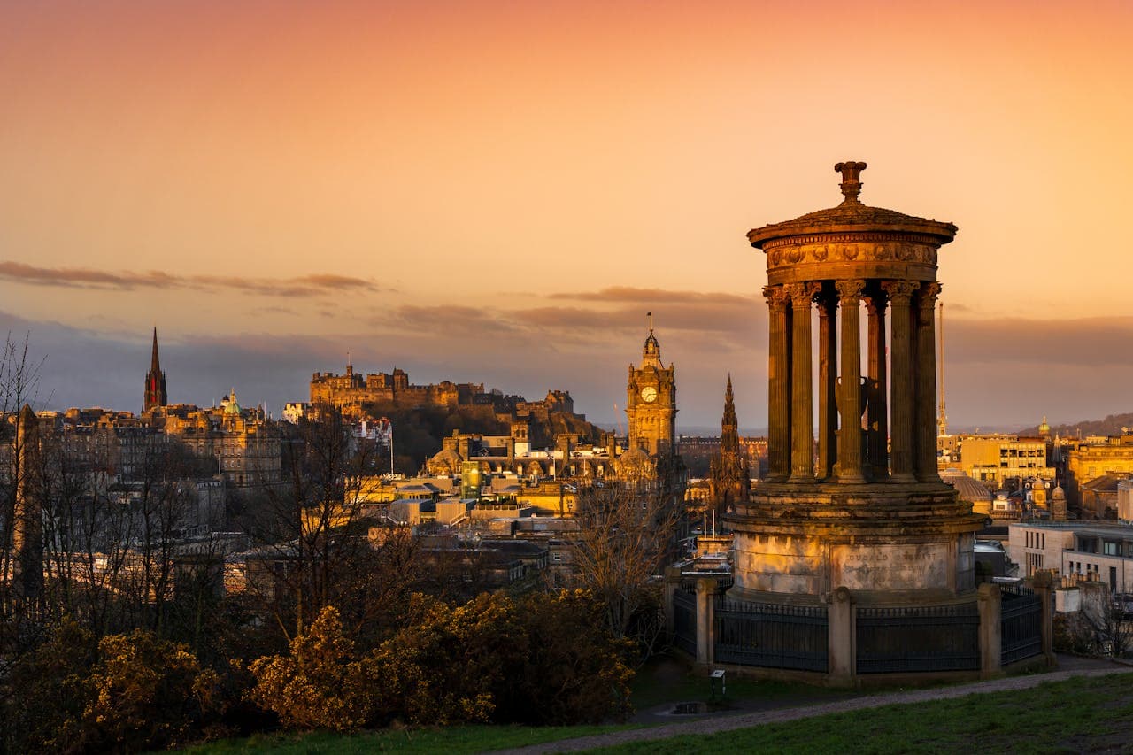 La silueta del reloj del Hotel Balmoral y el Castillo de Edimburgo iluminados al caer el sol desde Calton Hill.