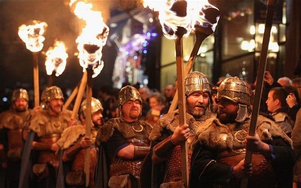 Personajes caracterizados con pinturas corporales y trajes celtas portando antorchas de fuego en la noche de Edimburgo.