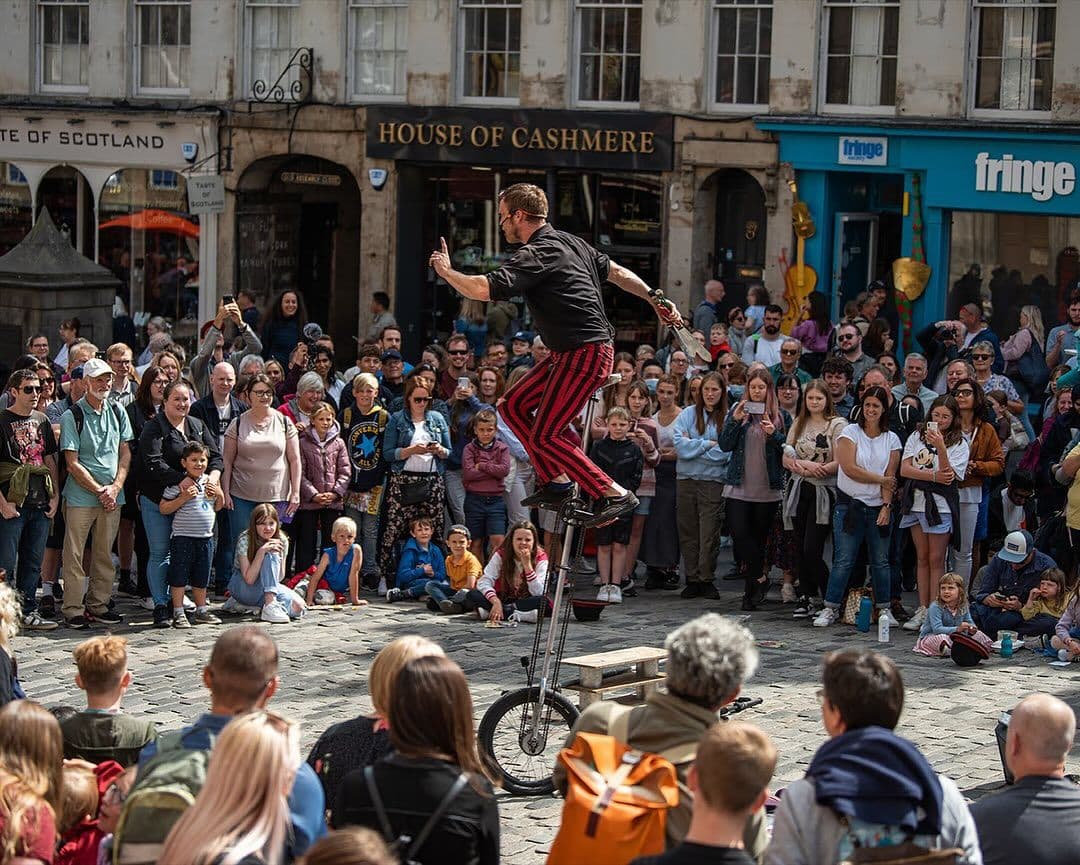 Spectacular street performer juggling on a high unicycle in front of a massive crowd on the Royal Mile.