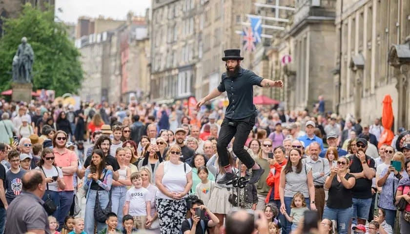 Crowded Royal Mile filled with street performers, tourists, and colorful posters during the Edinburgh Festival Fringe.