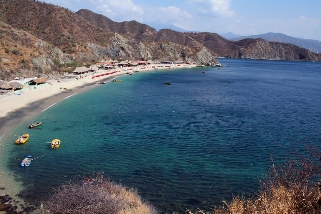Playa Blanca in Santa Marta, Colombia, viewed from the sea with arid hills and crystal-clear waters.