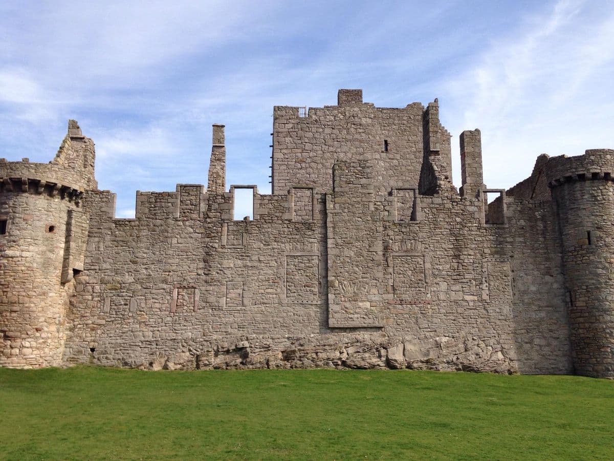 Vista exterior de las imponentes murallas medievales y la torre del homenaje del Castillo de Craigmillar en un día despejado.