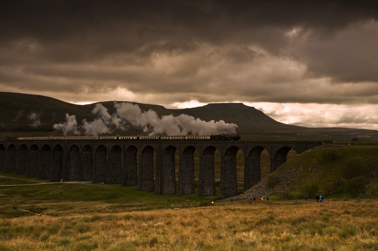 El tren de vapor Jacobite cruzando el viaducto de Glenfinnan rodeado de montañas en Escocia.