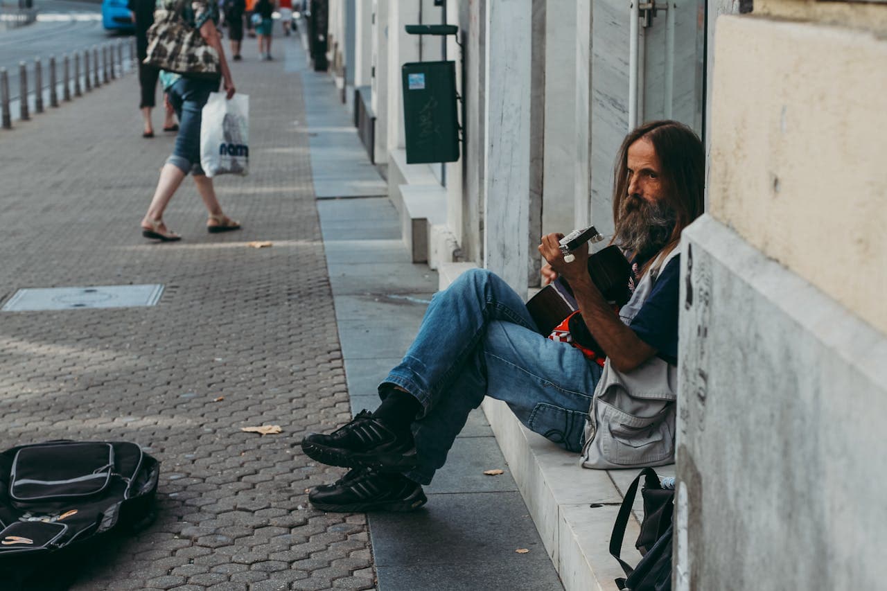 Street musician with a guitar sitting on a sidewalk in downtown Zagreb, Croatia.
