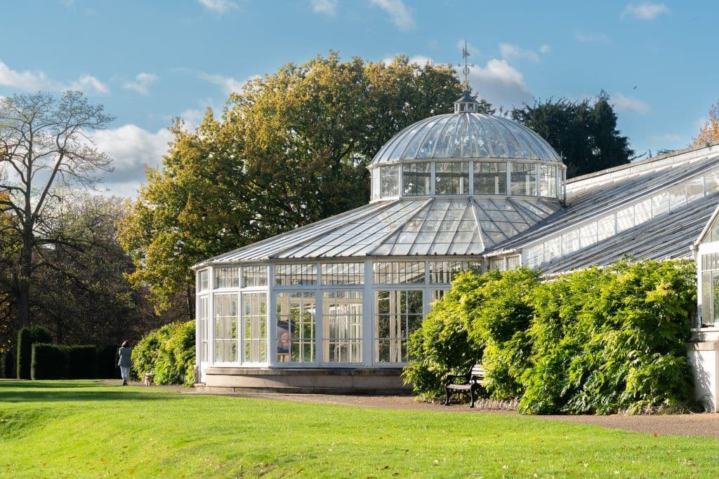 The spectacular Kibble Palace glasshouse illuminated by the sun among the lawns of the Glasgow Botanic Gardens.