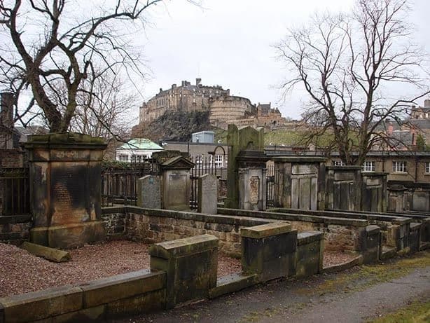 Las antiguas lápidas de piedra de Greyfriars Kirkyard con el Castillo de Edimburgo recortándose al fondo.