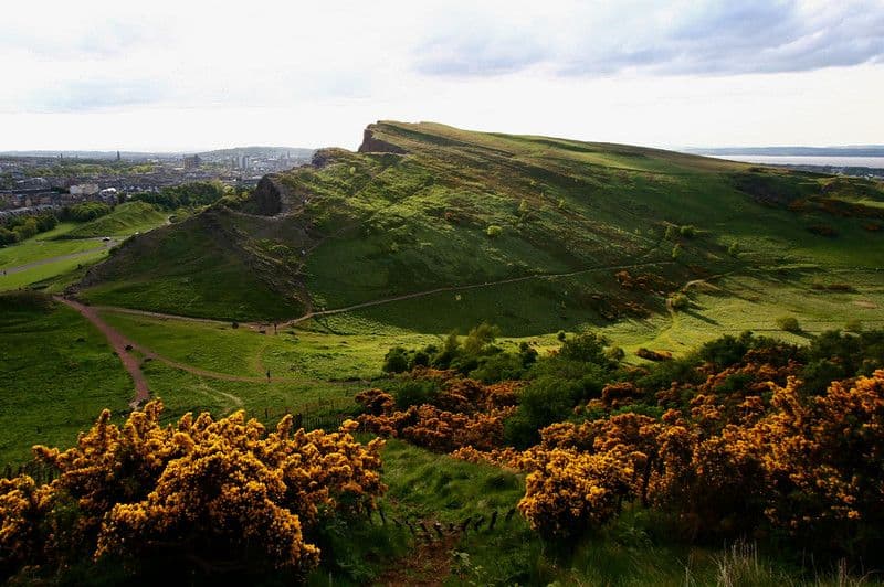 Vista panorámica de las colinas de Holyrood Park con los acantilados de Salisbury Crags bajo un cielo nublado escocés.