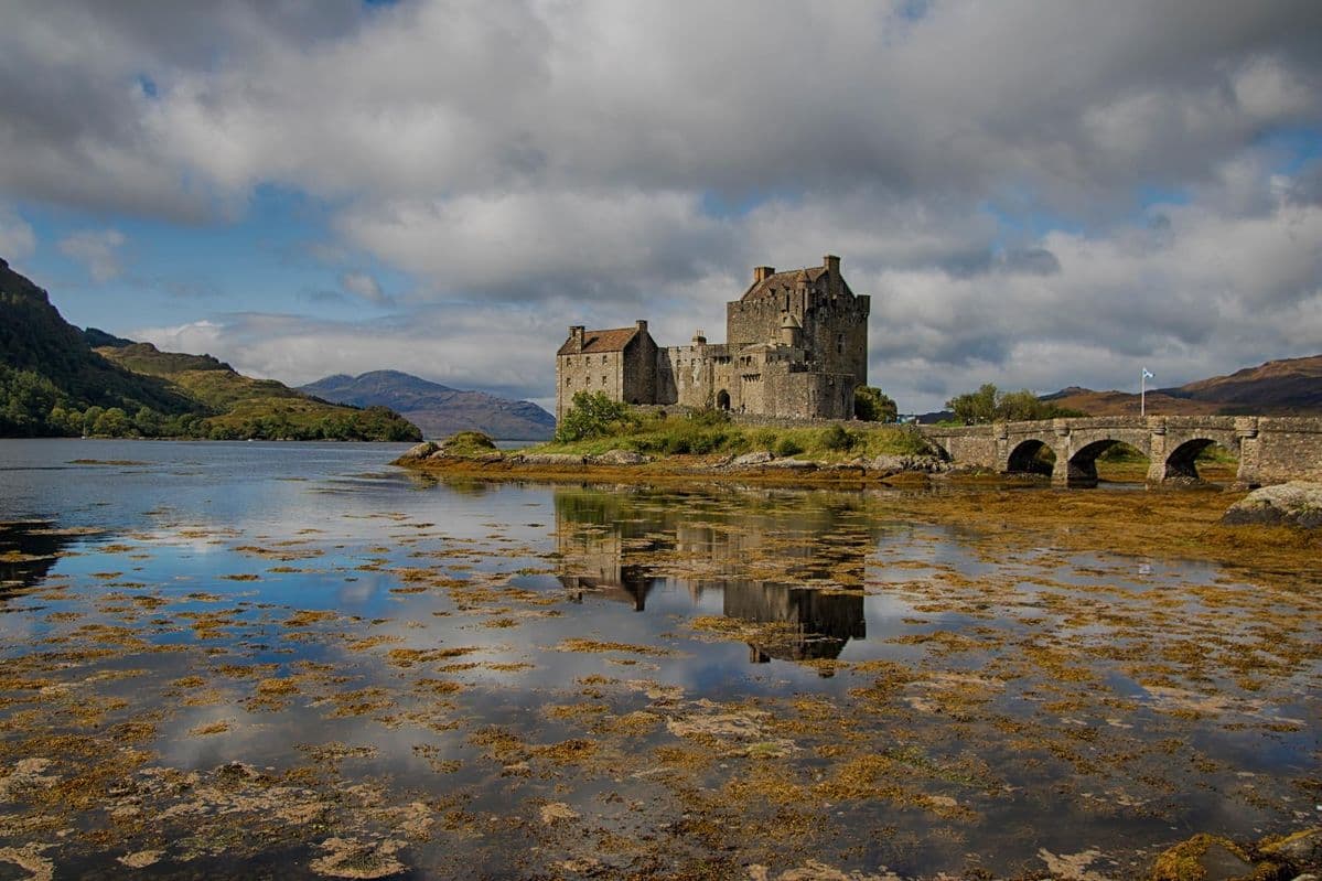 El Castillo de Eilean Donan reflejado sobre el agua en un día nublado en las Highlands de Escocia.