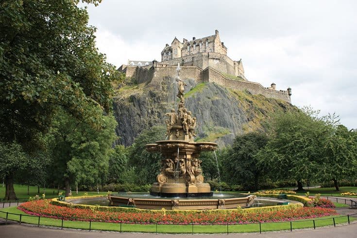 La histórica Fuente Ross de hierro fundido en primer plano con el imponente Castillo de Edimburgo sobre el acantilado al fondo.