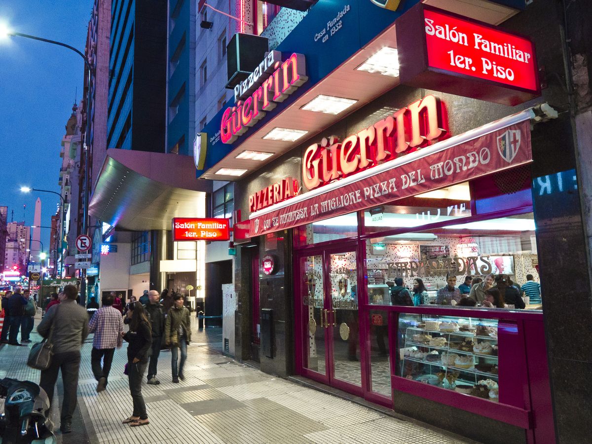 Fachada iluminada e salão da histórica pizzaria Güerrin na Avenida Corrientes, em Buenos Aires.