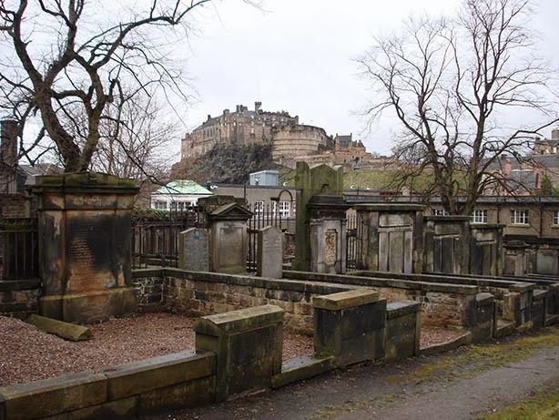 As antigas lápides de pedra do Greyfriars Kirkyard com o Castelo de Edimburgo recortando-se ao fundo.