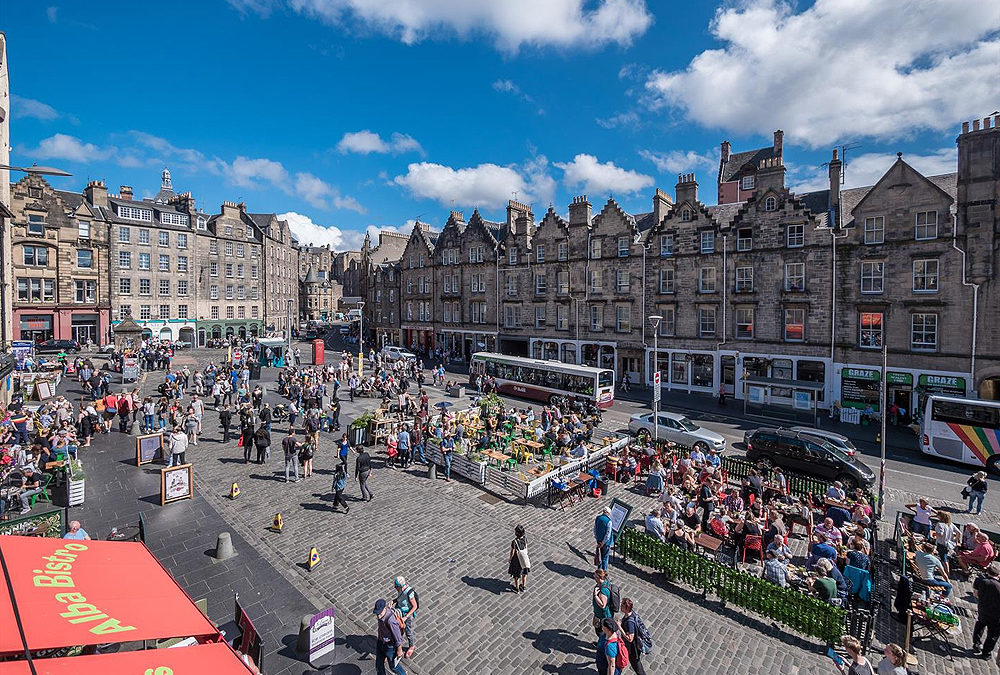 Vista panorâmica da praça do Grassmarket com suas fachadas coloridas de lojas e pubs, em Edimburgo, Escócia.