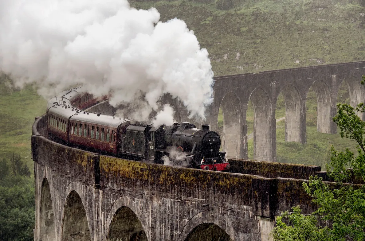 O trem a vapor Jacobite cruzando o viaduto de Glenfinnan cercado por montanhas na Escócia.