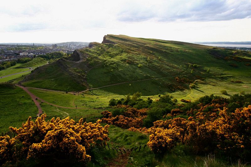 Panoramic view of the Holyrood Park hills with the Salisbury Crags cliffs under a cloudy Scottish sky.