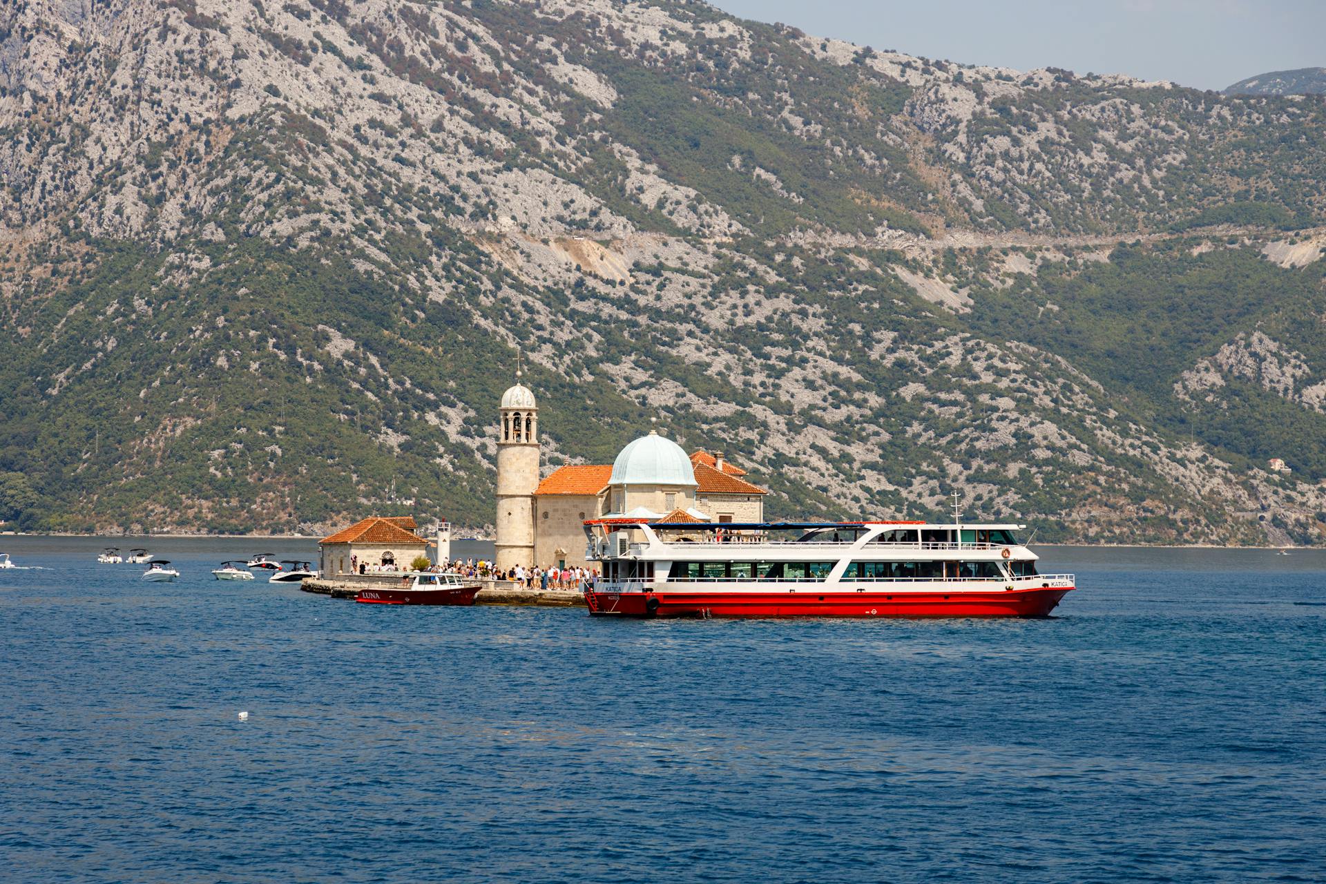 Ferry turístico cerca de Nuestra Señora de las Rocas en Perast, Montenegro con un pintoresco telón de fondo de montaña.