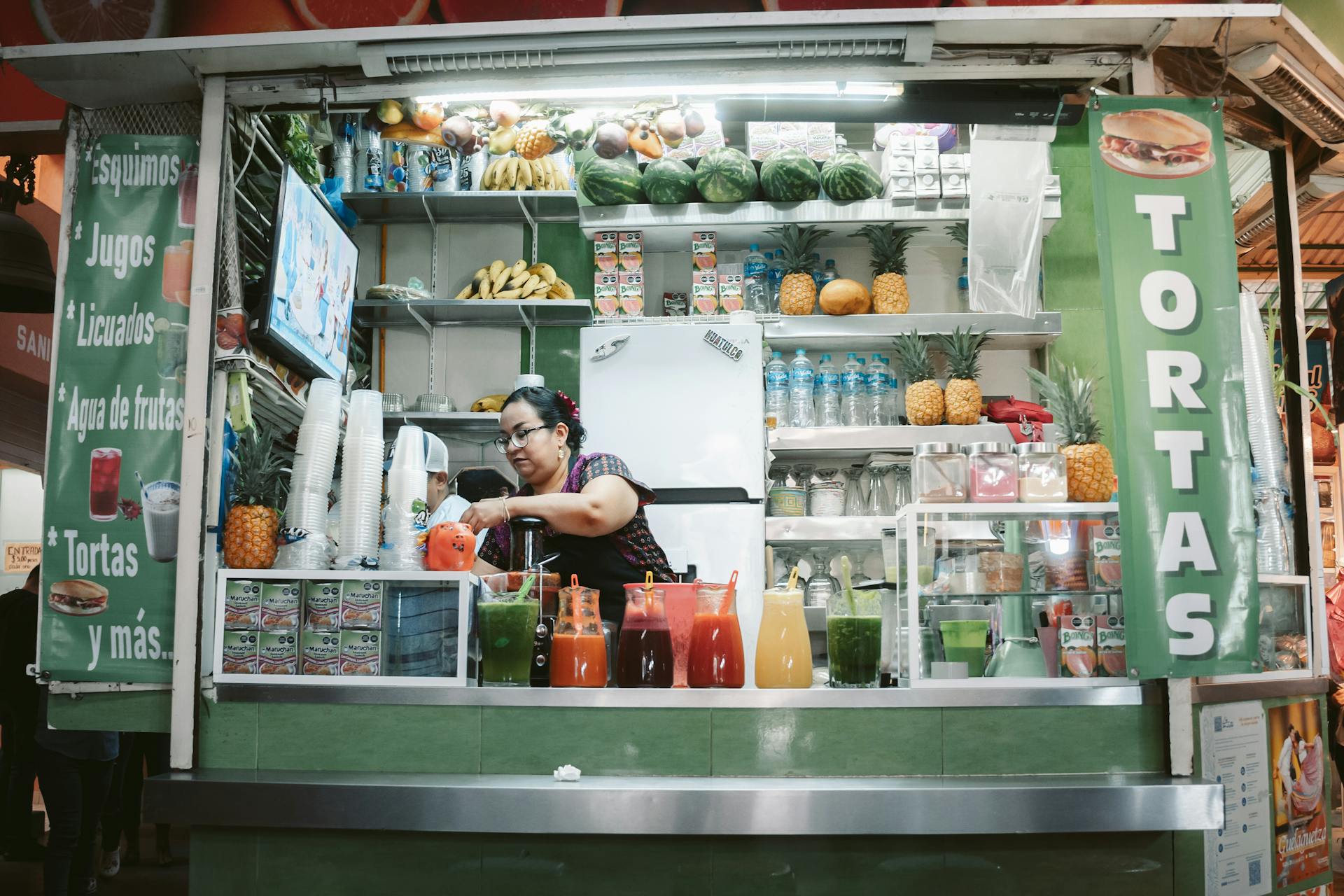 Puesto de jugos colorido con frutas frescas y bebidas en un mercado en México.