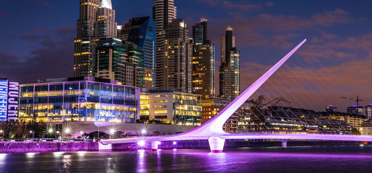 Illuminated night view of Puente de la Mujer in Puerto Madero with reflections on the water.