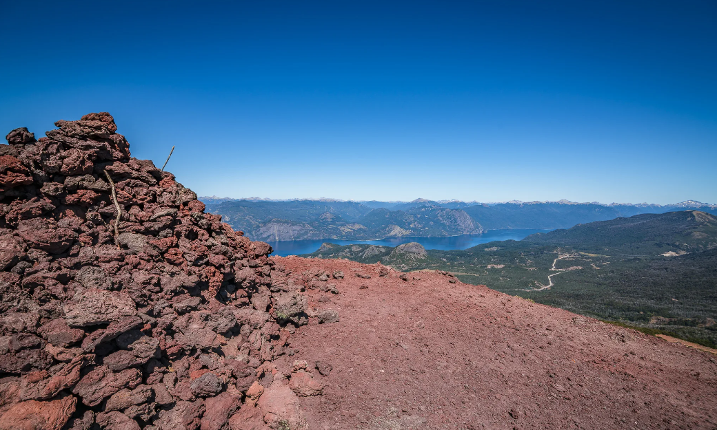 Hikers ascending towards the summit of Cerro Colorado with expansive mountain views and red volcanic soils.