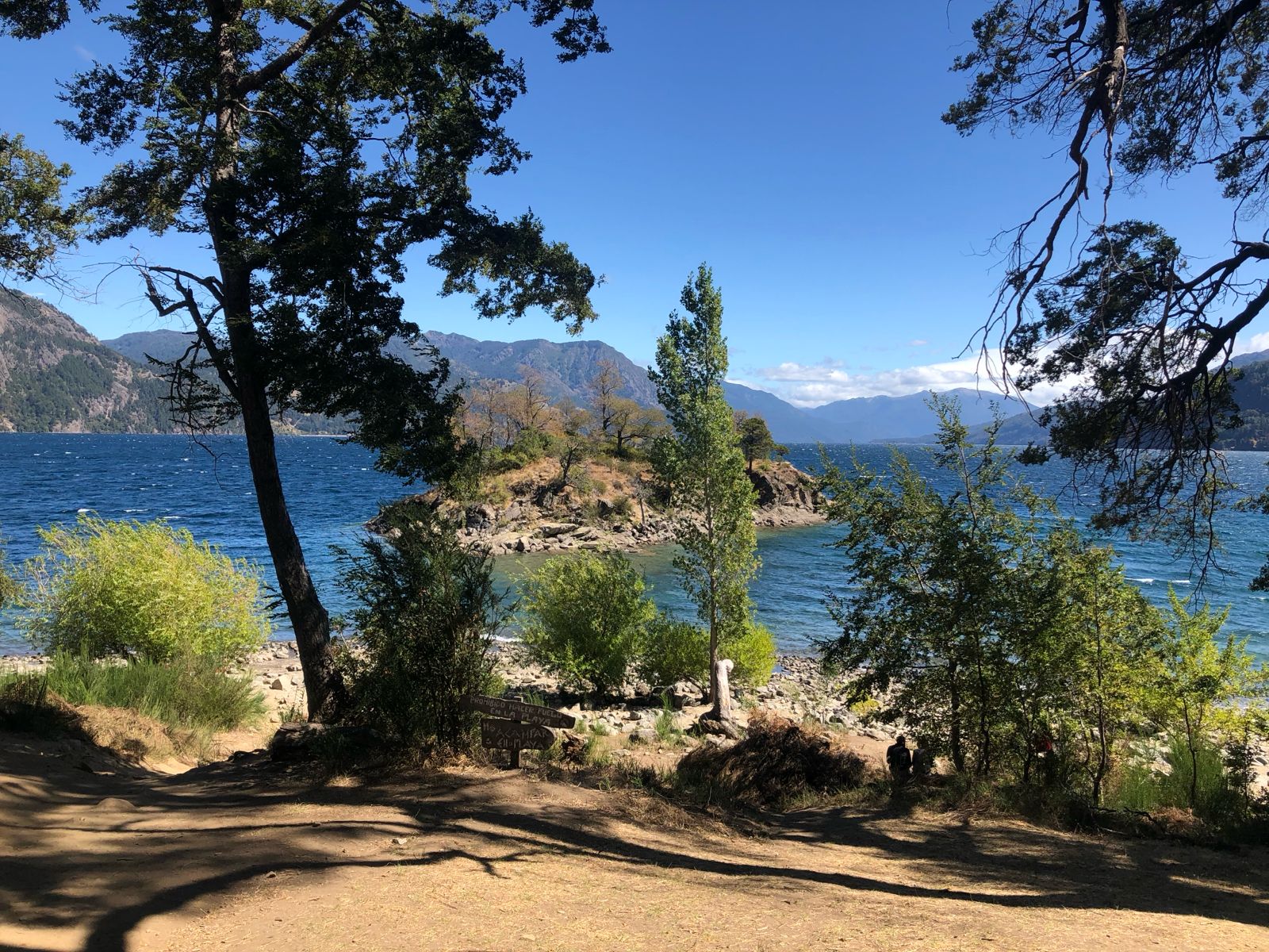The sandy shore of La Islita beach with its iconic small tree-covered island just a few meters away in Lake Lácar.